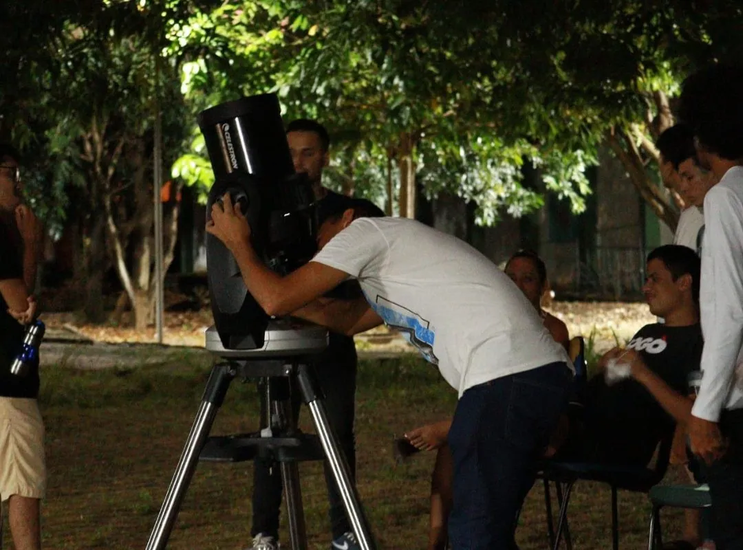 Estudante observa o eclipse lunar por um telescópio no Campus Imperatriz, com outros acadêmicos ao redor